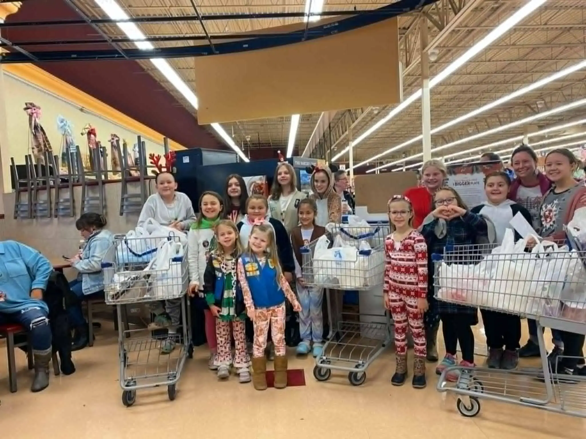 A Girl Scout troop standing with shopping carts full of bagged groceries inside a supermarket.