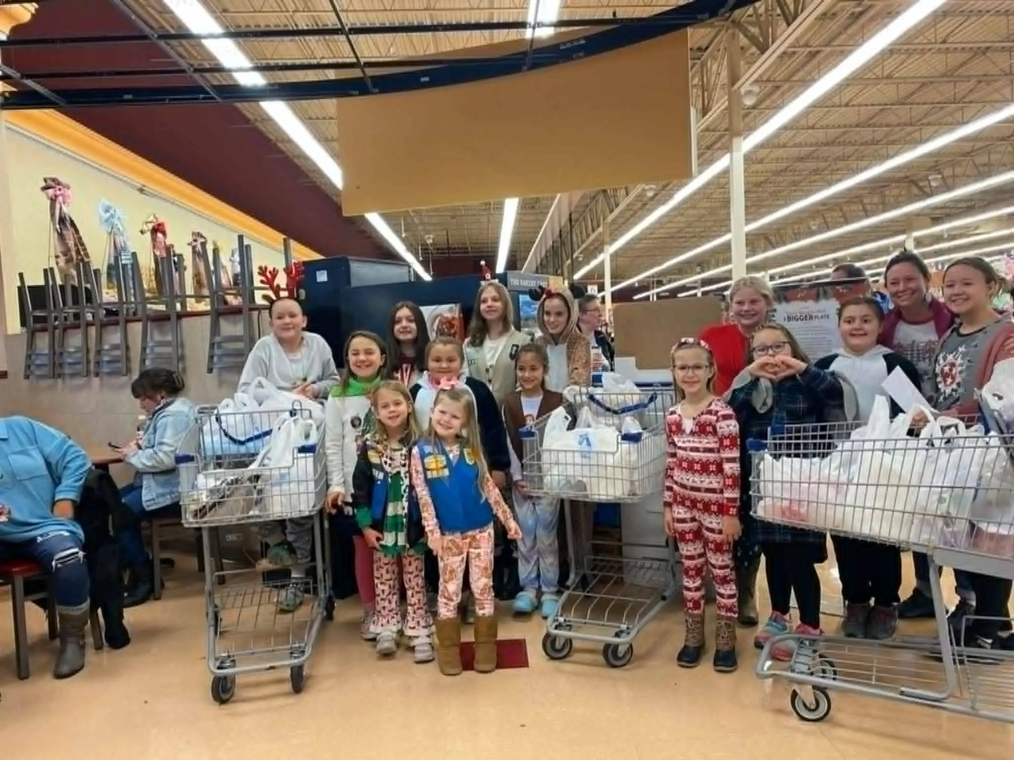 A Girl Scout troop standing with shopping carts full of bagged groceries inside a supermarket.