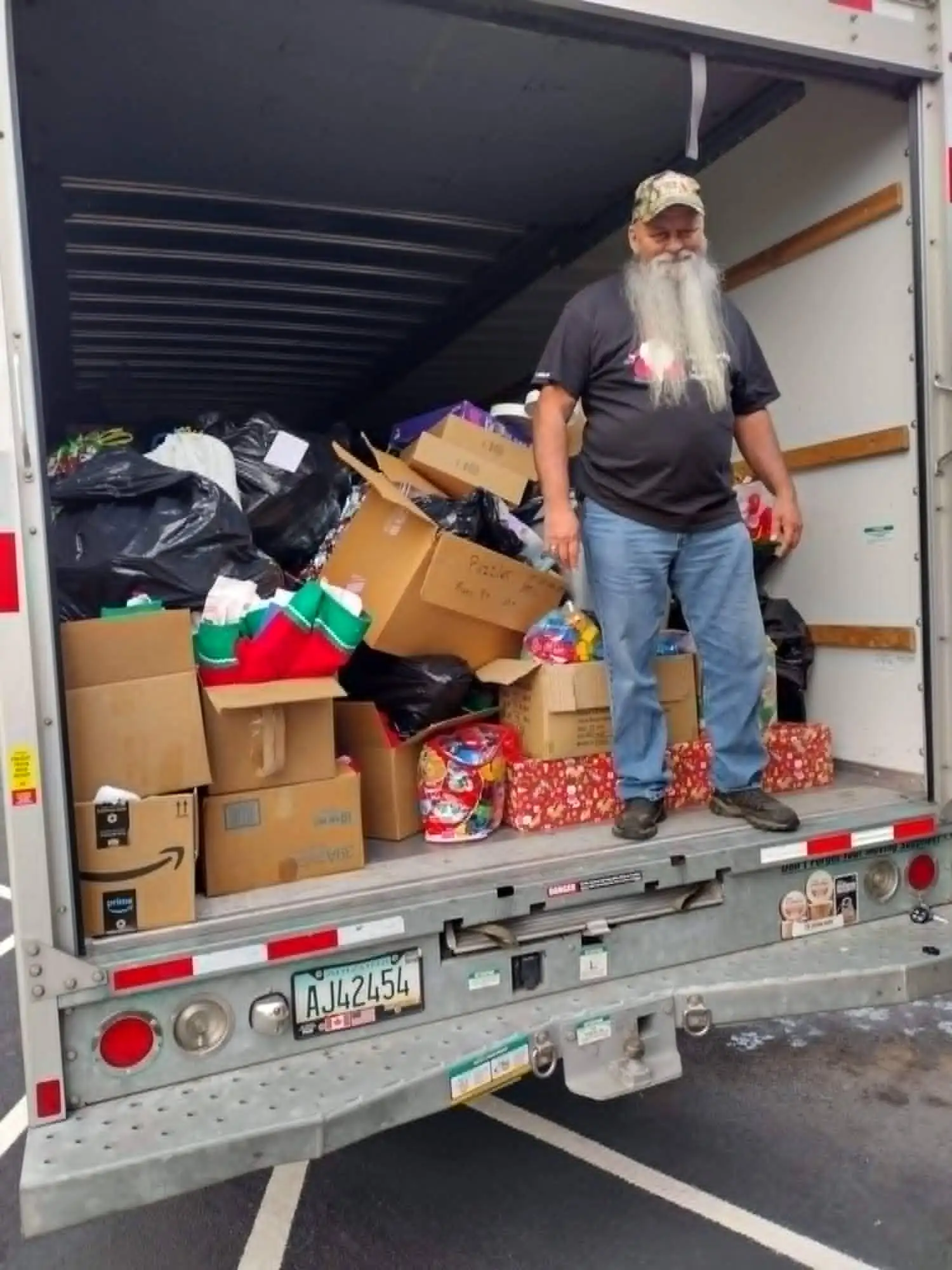 A volunteer standing in the back of a box truck filled with donated boxes, bags, and wrapped gifts.