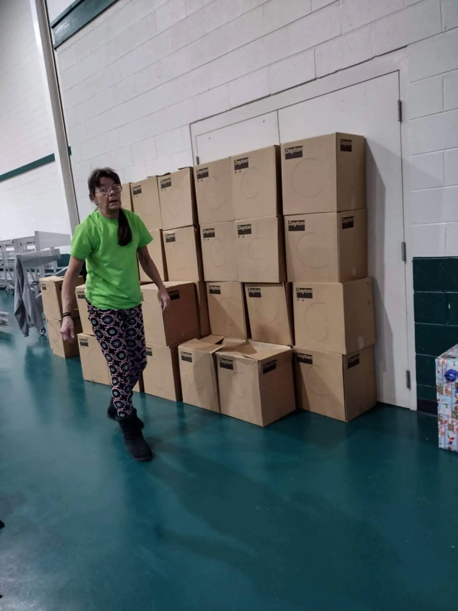 A volunteer standing beside a wall of packed food boxes stacked three high.