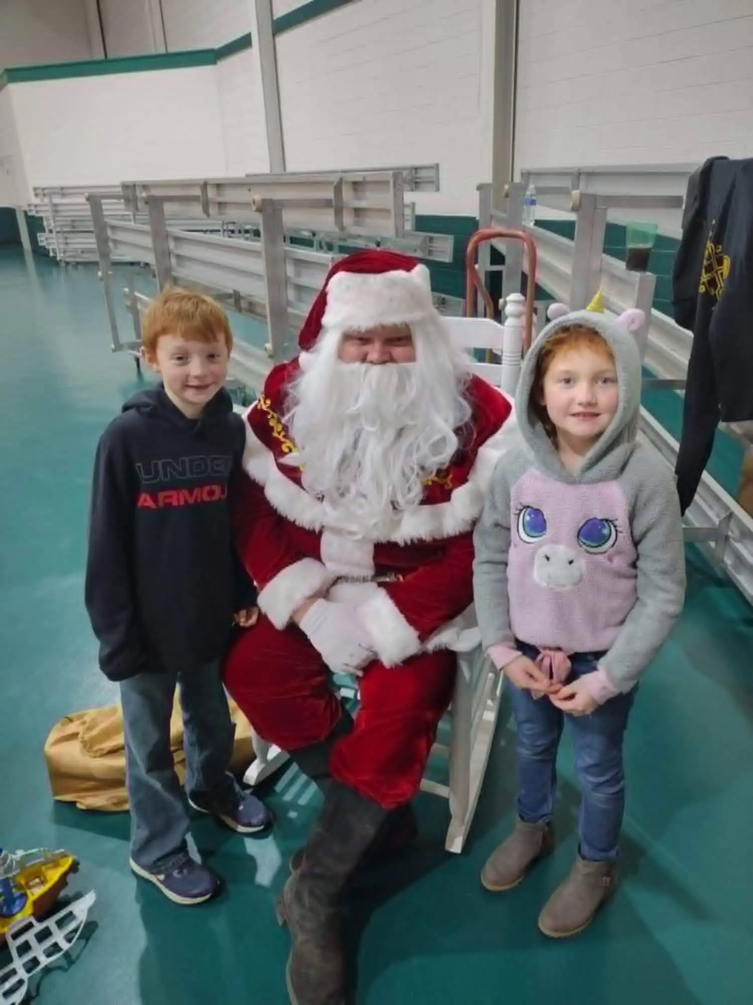 Santa seated in a rocking chair with two children standing on either side of him.