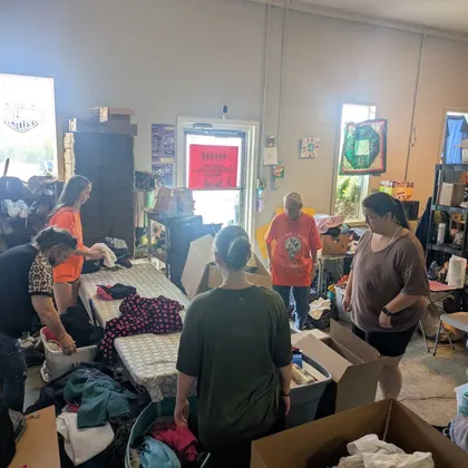 Volunteers sorting donated clothing into bins and boxes around a long table inside the Hunger First building.